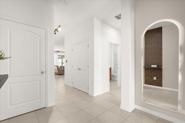 hall with visible vents, a high ceiling, arched walkways, and light tile patterned floors