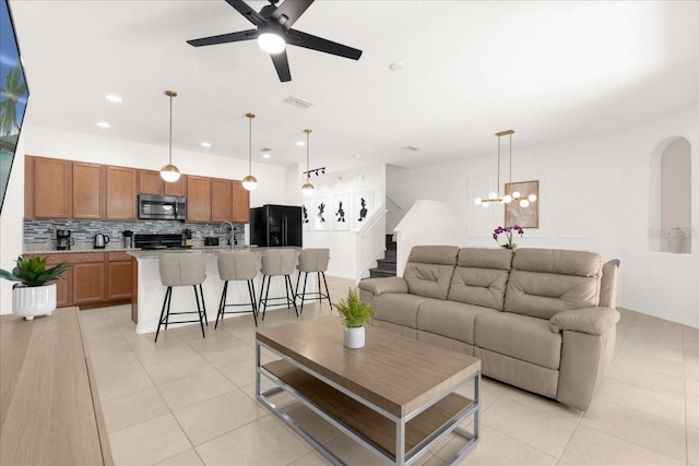 living area featuring light tile patterned flooring, visible vents, stairs, recessed lighting, and ceiling fan with notable chandelier