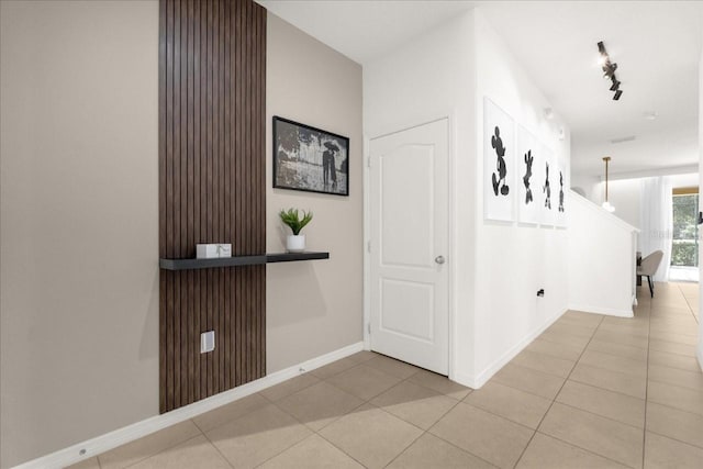 hall with baseboards, rail lighting, and light tile patterned floors