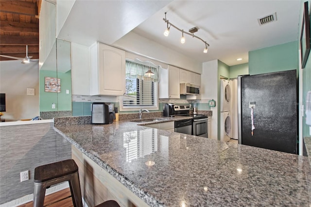 kitchen with visible vents, dark stone counters, stainless steel appliances, and stacked washing maching and dryer