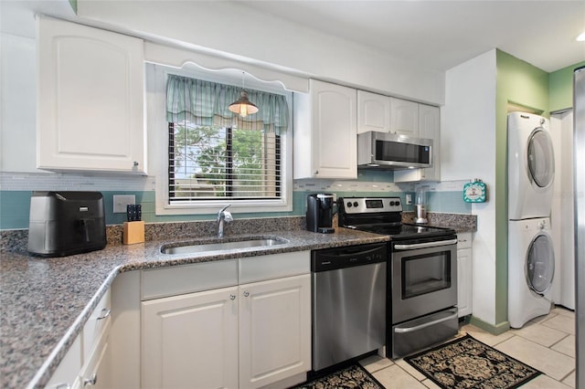 kitchen featuring stacked washer and dryer, a sink, backsplash, appliances with stainless steel finishes, and white cabinets
