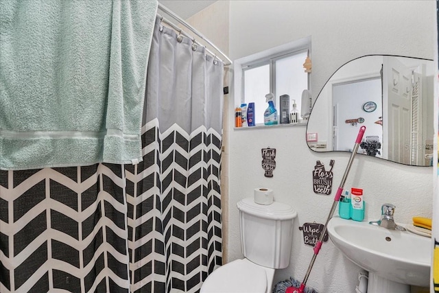 bathroom featuring toilet, a shower with shower curtain, a textured wall, and a sink
