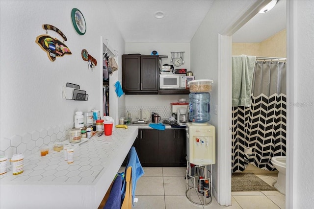 kitchen with white microwave, dark brown cabinetry, light tile patterned flooring, light countertops, and a sink