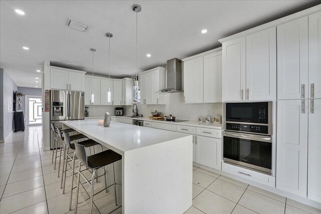 kitchen with appliances with stainless steel finishes, light tile patterned floors, wall chimney range hood, and a kitchen breakfast bar