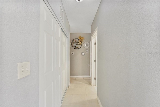 hall featuring light tile patterned floors, a textured wall, and visible vents