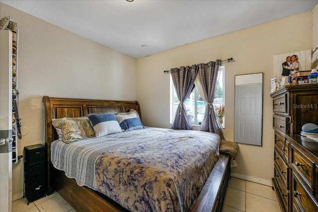 bedroom featuring a textured wall, baseboards, and light tile patterned flooring