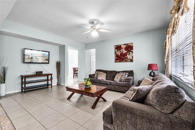 living room with light tile patterned flooring, a textured ceiling, baseboards, and ceiling fan