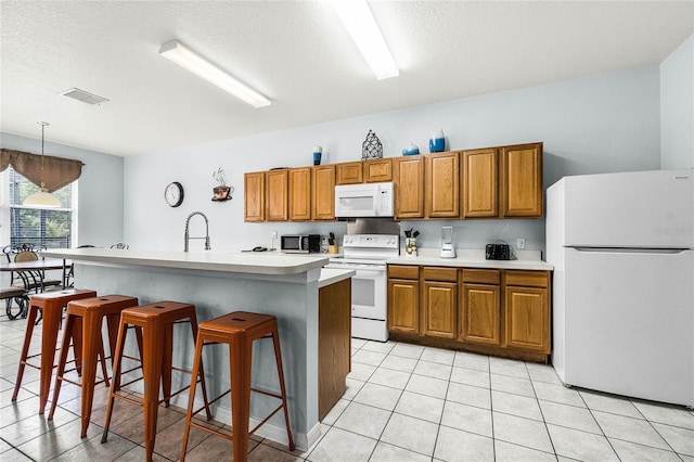 kitchen with light countertops, visible vents, white appliances, brown cabinets, and a breakfast bar area