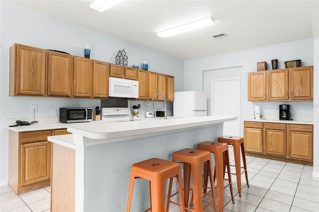 kitchen featuring light countertops, a breakfast bar area, white appliances, a sink, and visible vents