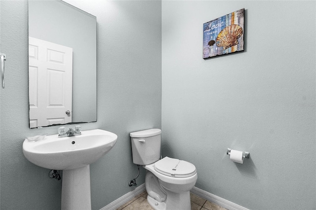 half bath featuring tile patterned floors, toilet, and baseboards