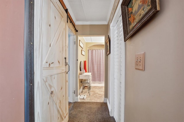 corridor featuring a barn door, carpet flooring, and crown molding