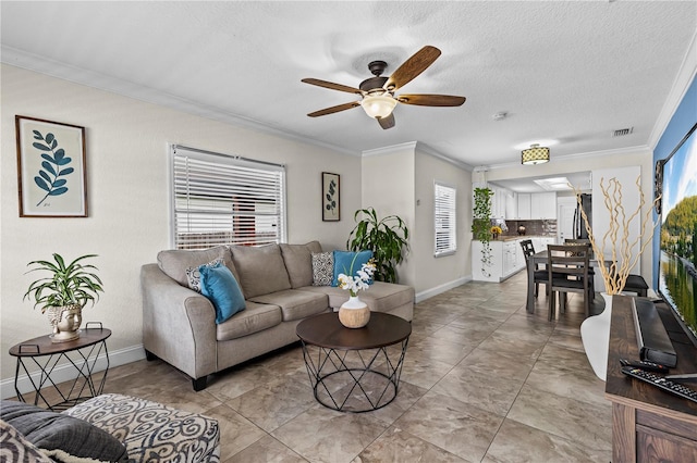 living room featuring a textured ceiling, baseboards, ornamental molding, and a ceiling fan