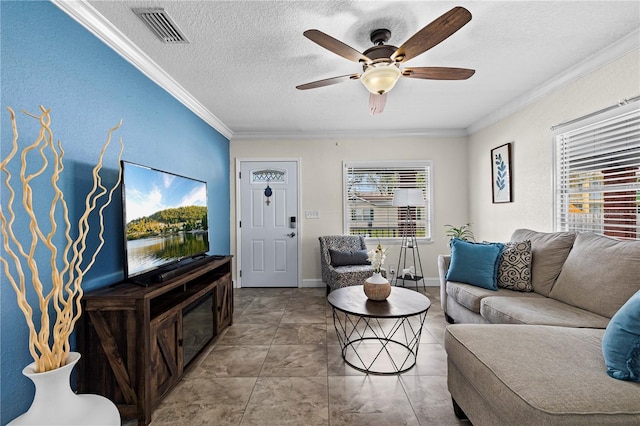 living area with a textured ceiling, visible vents, crown molding, baseboards, and ceiling fan