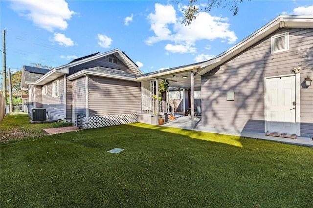 rear view of property with central air condition unit, fence, a patio, solar panels, and a lawn
