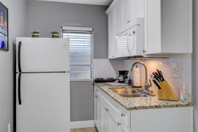 kitchen featuring decorative backsplash, white cabinets, white appliances, light stone countertops, and a sink