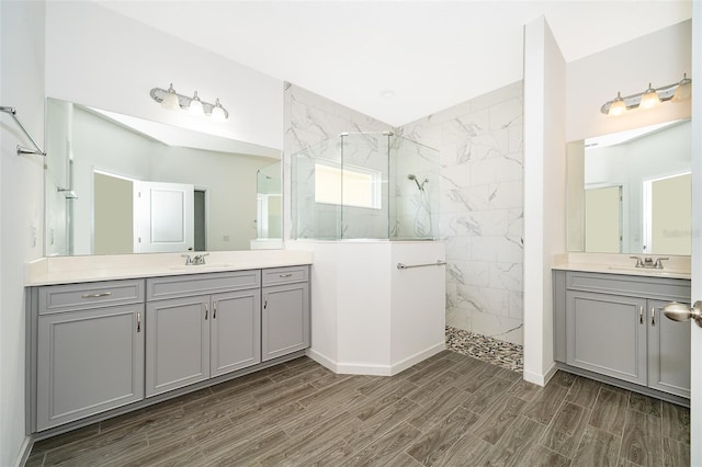 full bath featuring wood tiled floor, two vanities, a sink, and a marble finish shower