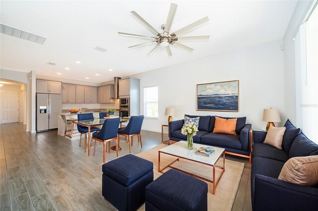 living room with visible vents, recessed lighting, a ceiling fan, arched walkways, and light wood-type flooring