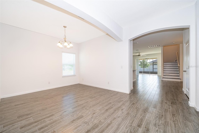 empty room featuring stairway, ceiling fan with notable chandelier, arched walkways, visible vents, and wood finished floors