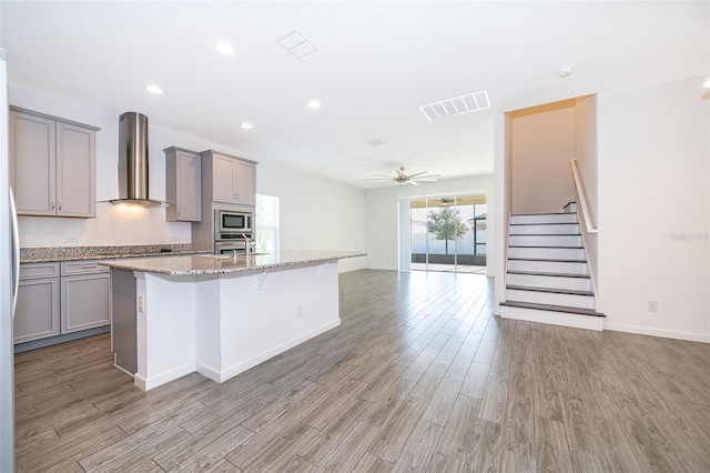 kitchen featuring visible vents, wall chimney range hood, gray cabinets, and appliances with stainless steel finishes