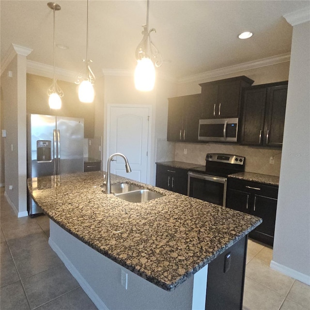kitchen with crown molding, dark stone counters, a center island with sink, appliances with stainless steel finishes, and a sink
