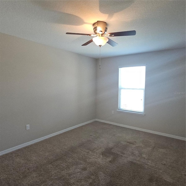 spare room featuring baseboards, dark colored carpet, and a ceiling fan