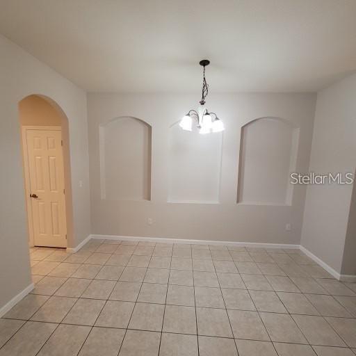 3351 Whitestone Cir Unit 101, Kissimmee, FL 34741 - unfurnished room with baseboards, arched walkways, light tile patterned flooring, and a notable chandelier