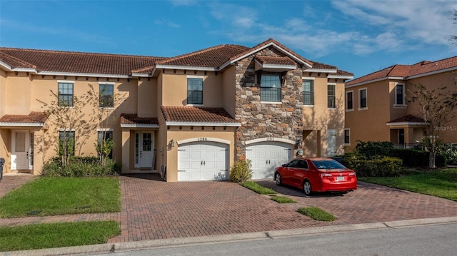 mediterranean / spanish-style home featuring a tile roof, driveway, stone siding, stucco siding, and a garage