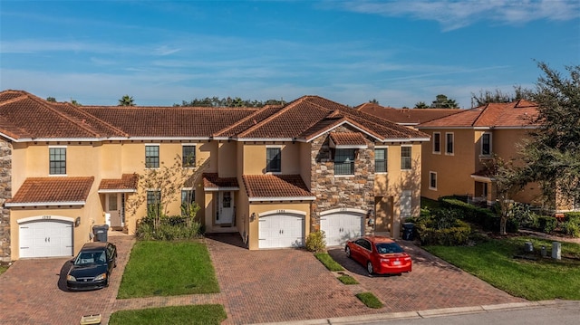 view of front of property with stucco siding, stone siding, a tiled roof, driveway, and a garage