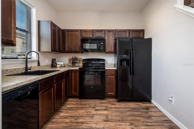 kitchen featuring light countertops, dark wood-type flooring, a sink, dark brown cabinetry, and black appliances