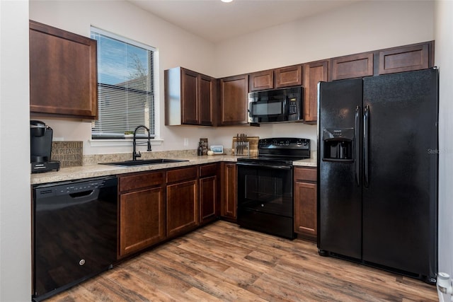 kitchen with light countertops, dark brown cabinetry, a sink, wood finished floors, and black appliances
