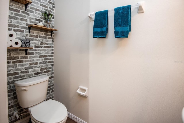 bathroom featuring baseboards, toilet, and brick wall