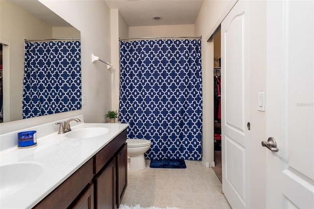 bathroom with double vanity, toilet, a sink, and a textured ceiling