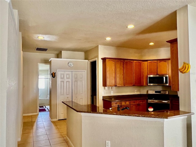 2920 River Birch Dr, Kissimmee, FL 34741 - kitchen with a textured ceiling, visible vents, brown cabinets, stainless steel appliances, and light tile patterned floors