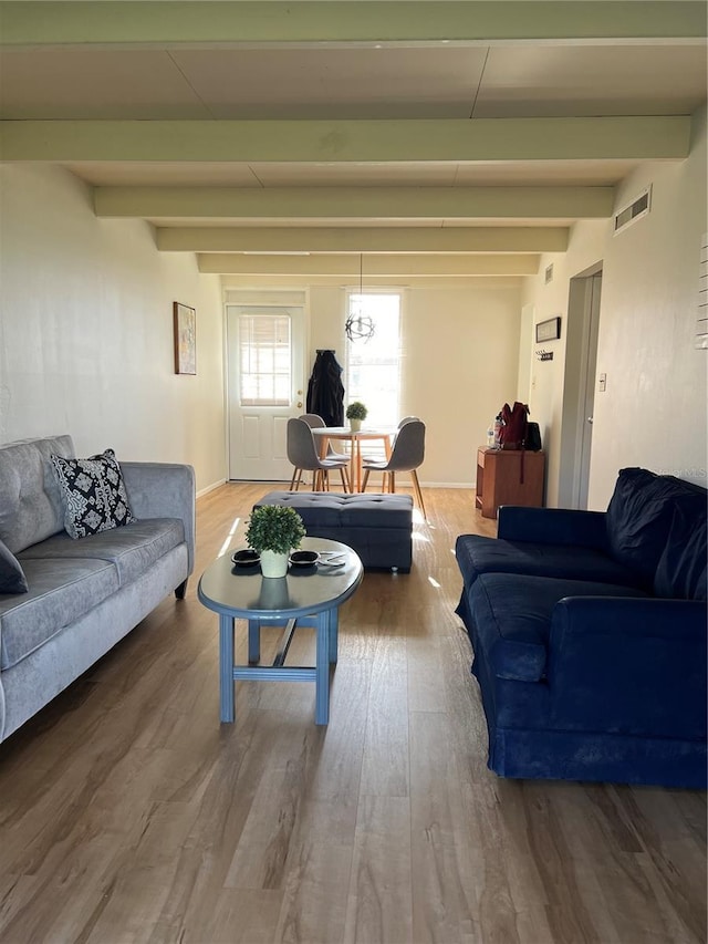 living area featuring visible vents, beam ceiling, and wood finished floors