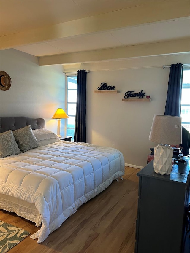 bedroom with wood finished floors, multiple windows, and beam ceiling