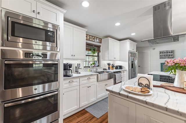 1999 Sir Lancelot Cir, Saint Cloud, FL 34772 - kitchen featuring island exhaust hood, wood finished floors, a sink, appliances with stainless steel finishes, and white cabinetry