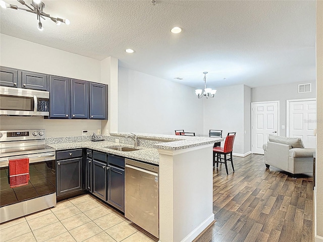 kitchen featuring stainless steel appliances, visible vents, a sink, a peninsula, and a chandelier