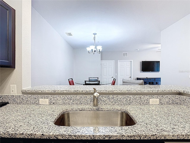 kitchen featuring a sink, a notable chandelier, and light stone counters