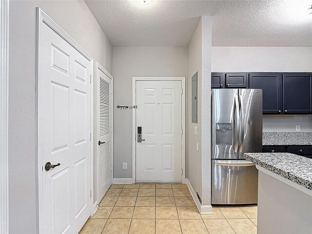 kitchen featuring dark cabinetry, light tile patterned floors, baseboards, a textured ceiling, and stainless steel refrigerator with ice dispenser