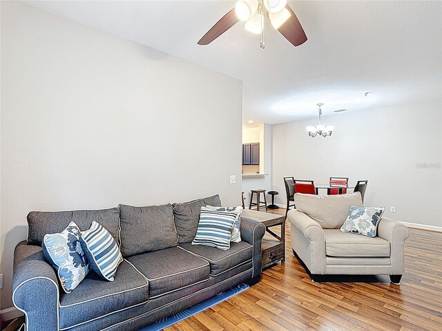 living area featuring baseboards, wood finished floors, visible vents, and ceiling fan with notable chandelier