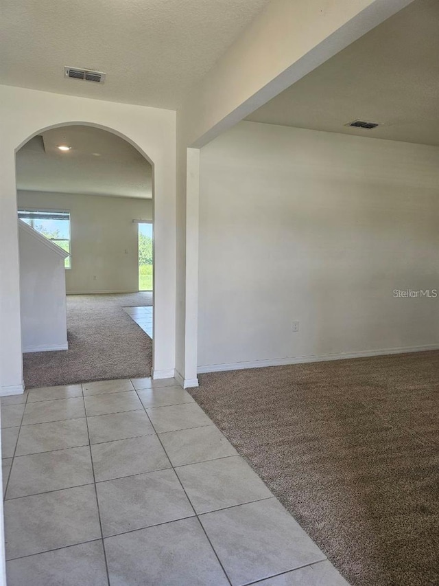 carpeted spare room with arched walkways, visible vents, and baseboards