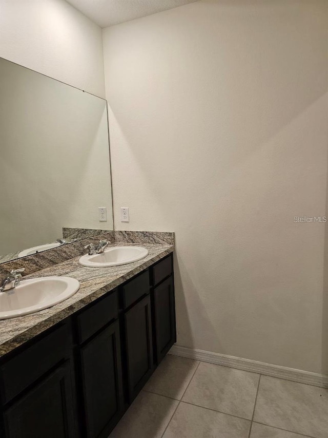 bathroom featuring tile patterned floors, double vanity, a sink, and baseboards