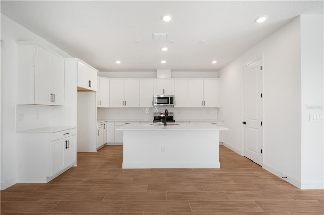 9143 Players Dr, Weeki Wachee, FL 34613 - kitchen with stainless steel appliances, light wood finished floors, light countertops, a center island with sink, and white cabinetry