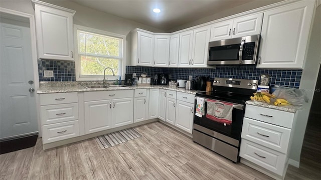 kitchen featuring white cabinets, a sink, stainless steel appliances, and light wood-type flooring