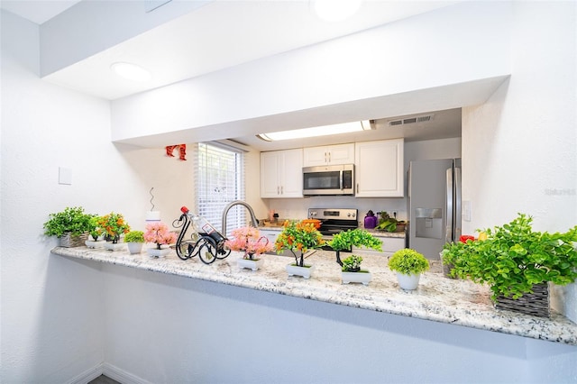 kitchen with stainless steel appliances, light stone countertops, a peninsula, and white cabinetry