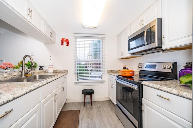 kitchen featuring baseboards, light wood-style flooring, white cabinetry, stainless steel appliances, and a sink