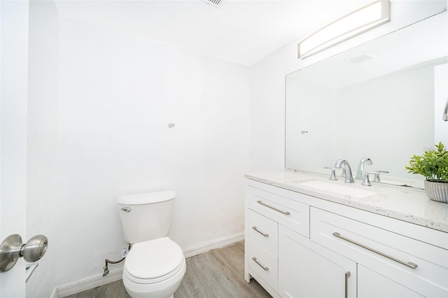 bathroom with toilet, vanity, wood finished floors, and baseboards