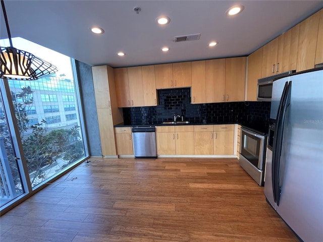 kitchen with wood finished floors, stainless steel appliances, dark countertops, light brown cabinets, and a sink
