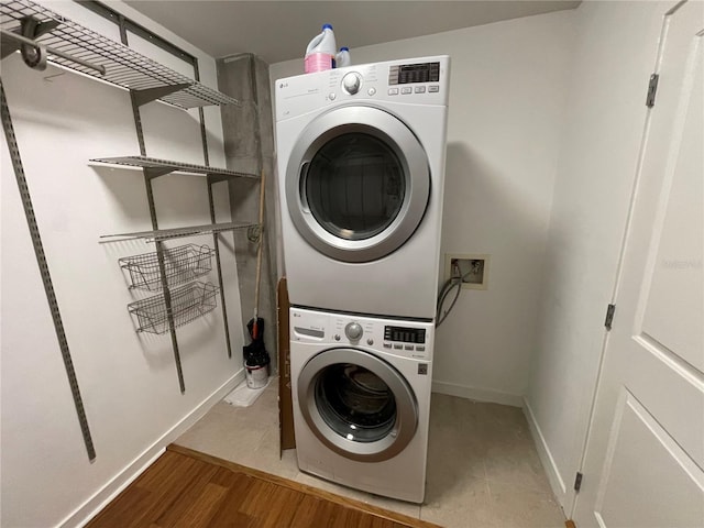 clothes washing area featuring stacked washer and dryer, baseboards, wood finished floors, and laundry area