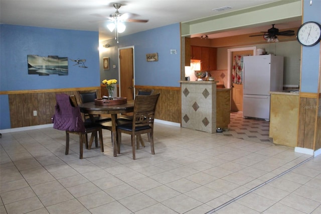 dining space featuring visible vents, light tile patterned floors, a ceiling fan, wooden walls, and wainscoting